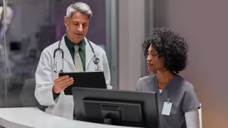 Two clinicians look at data on a desktop and tablet device.